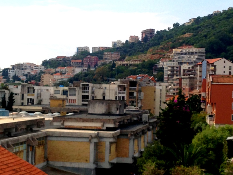 Panoramic view of residential buildings and green hills in Budva, Montenegro, overlooking the cityscape and landscape.