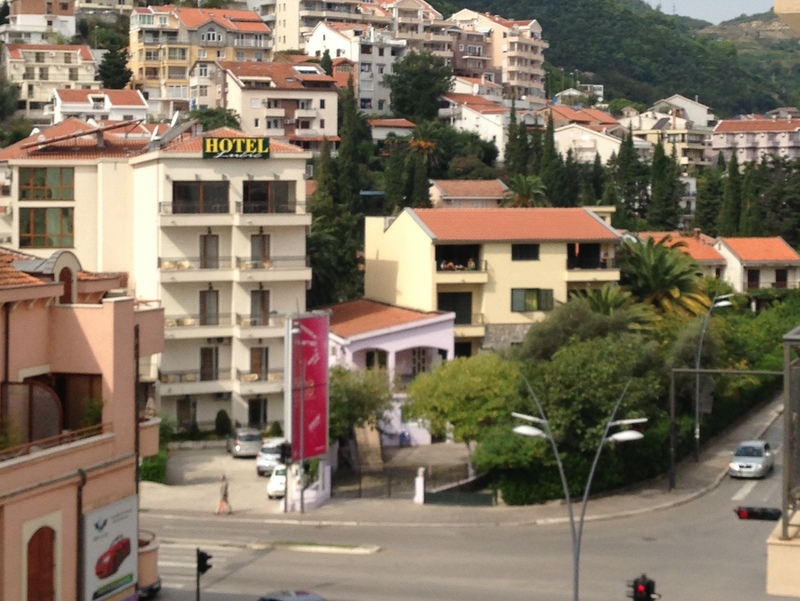 View of a hotel and residential buildings in Budva, Montenegro: urban development with red roofs, green trees, and a road.