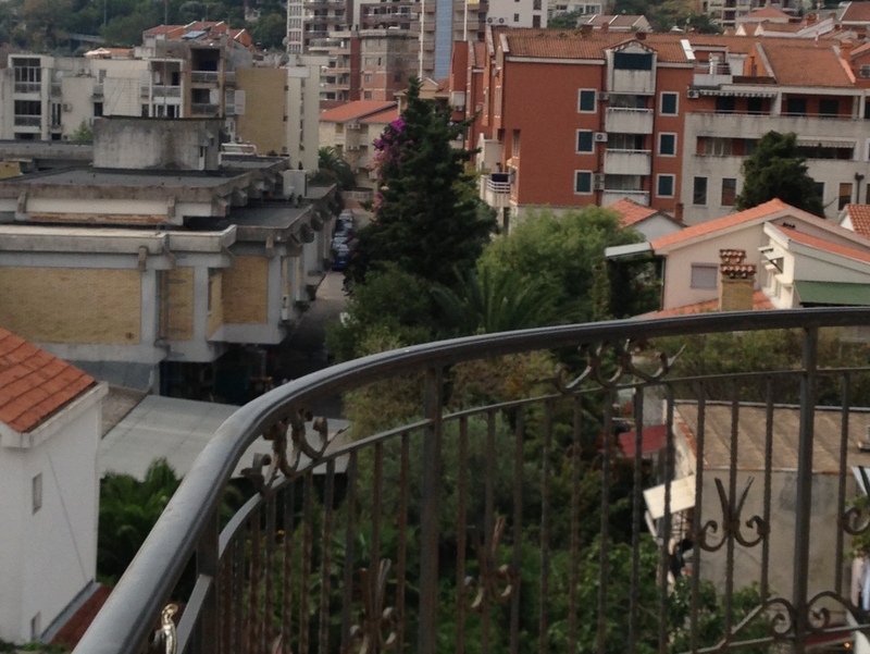 View from the balcony of city buildings and greenery in Budva, Montenegro: wrought-iron railing and a panorama of a residential neighborhood.