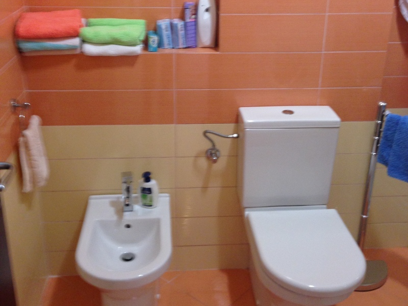 Bathroom in an apartment in Budva, Montenegro: white sanitary ware, bidet, toilet, and orange wall tiles.