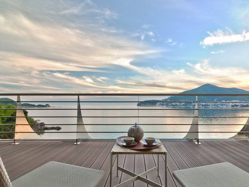 Balcony with sea and mountain views in Dukley, Bečići, Montenegro: decking, wicker furniture, and a tea set.