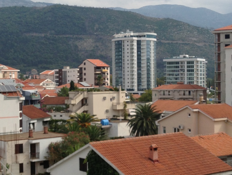 Panoramic view of residential buildings and modern high-rises in Budva, Montenegro, with mountains in the background.