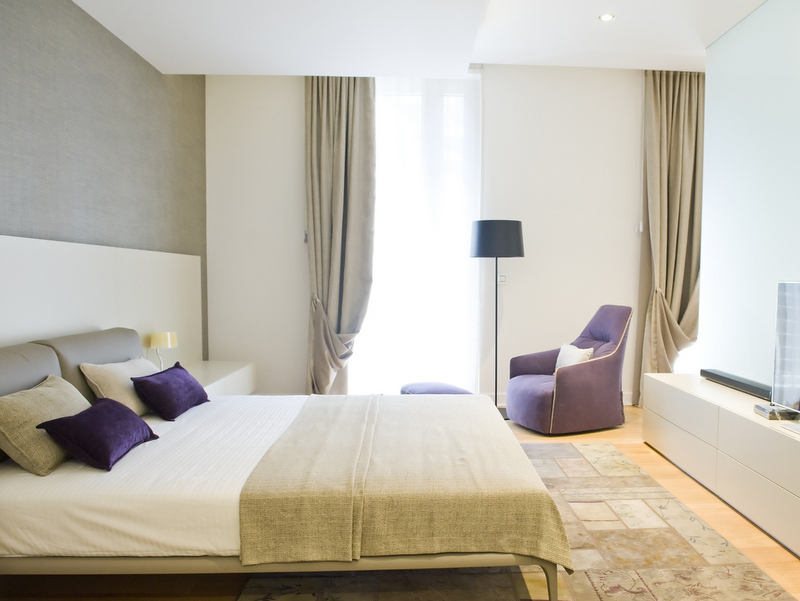 Modern bedroom in Dukley Gardens, Becici, Montenegro: double bed, purple armchair, and panoramic windows.