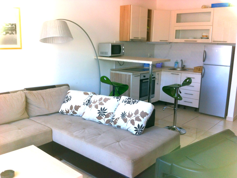 Living room with kitchen in an apartment in Bečići, Montenegro: corner sofa, bar counter, appliances, and light-colored furniture.