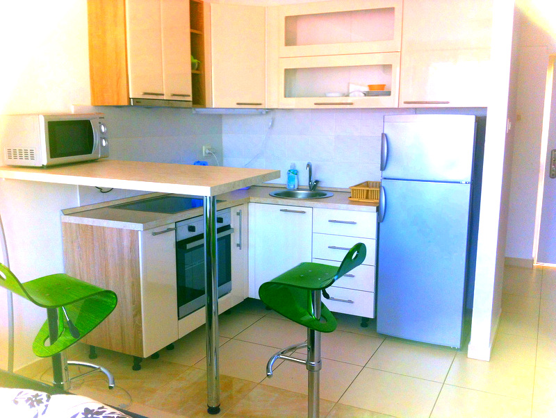 Modern kitchen in an apartment in Bečići, Montenegro: light cabinetry, a bar counter, and bright green chairs.