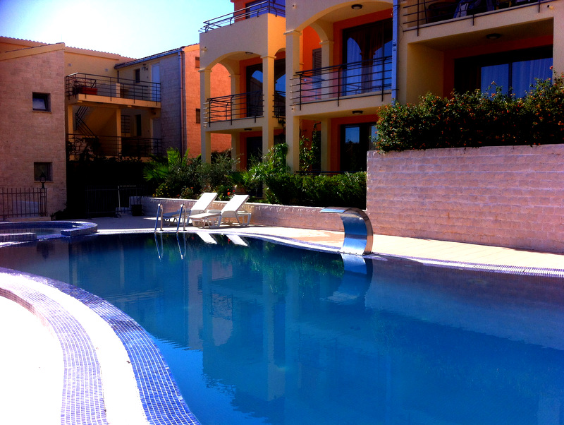 Outdoor pool with a waterfall at a residential complex in Bečići, Montenegro: sun loungers, a terrace, and a view of modern apartments.
