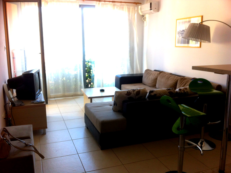 Living room in an apartment in Bečići, Montenegro: corner sofa, bar stools, light tile, and access to the balcony.