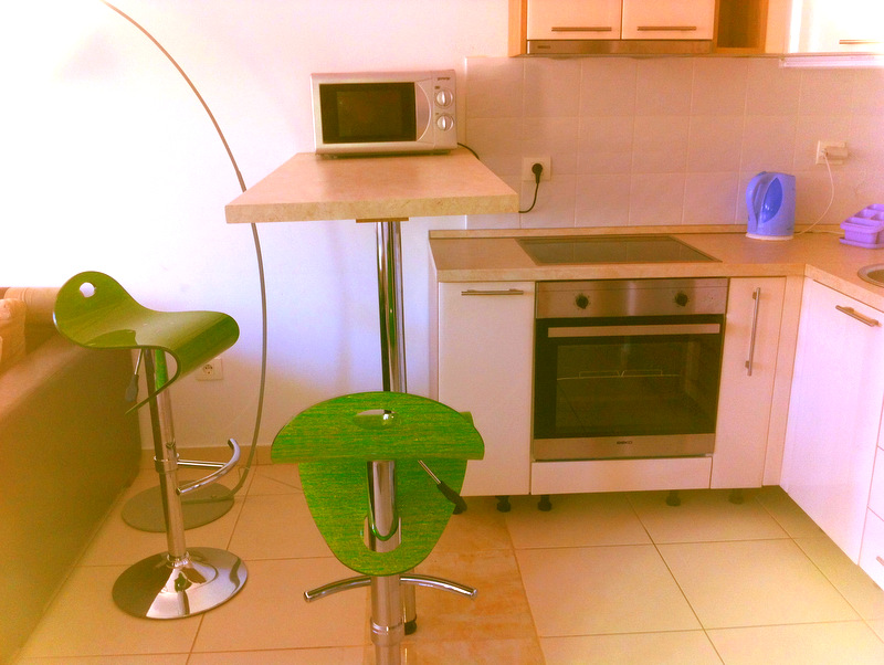 Kitchen in an apartment in Bečići, Montenegro: a bar counter, green chairs, built-in appliances, and light finishes.