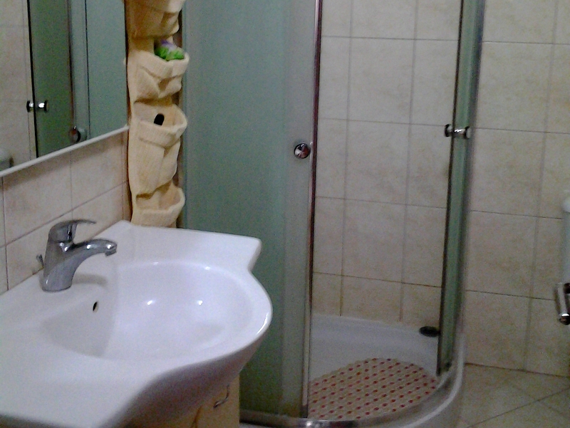 Bathroom in an apartment in Bar, Montenegro: light tiles, a shower cabin with frosted glass, and a white sink.
