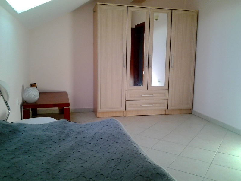 Bedroom in an apartment in Bar, Montenegro: a light wardrobe with mirrors, a bed with a gray bedspread, and a bedside table.