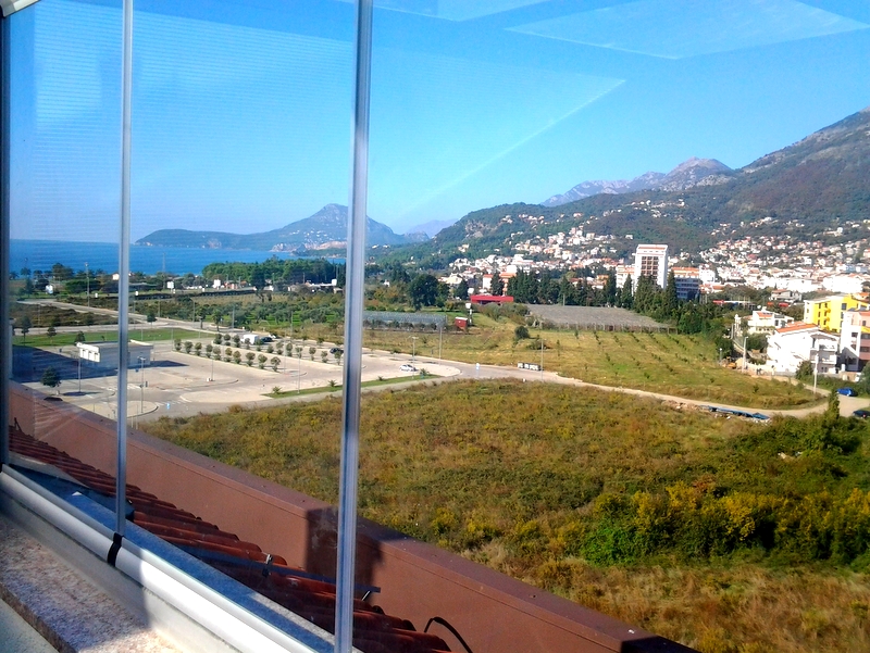 View from the apartment’s glazed balcony in Bar, Montenegro: a panorama of the sea, mountains, and city infrastructure.
