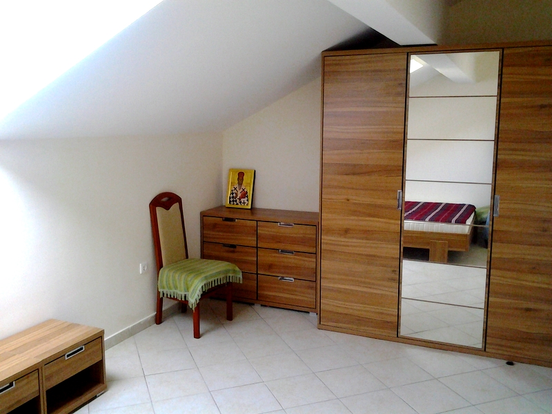 Bedroom in the apartment attic in Bar, Montenegro: wooden wardrobe with mirror, dresser, chair, and tiled floor.