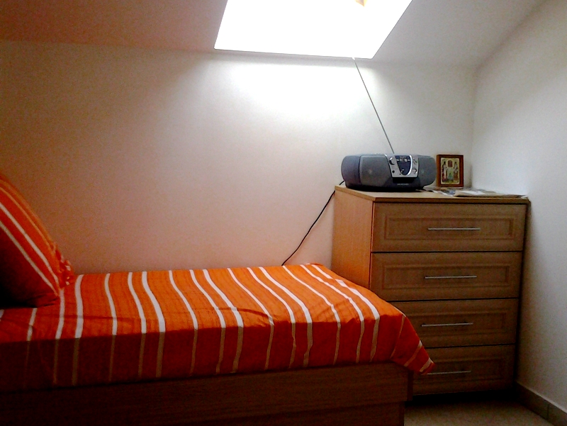 Bedroom in a loft apartment in Bar, Montenegro: a single bed with an orange bedspread and a dresser under the window.