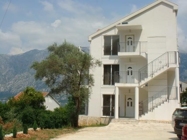 Three-story residential building with external staircases and mountain views in Stoliv, Montenegro. Building facade with balconies.
