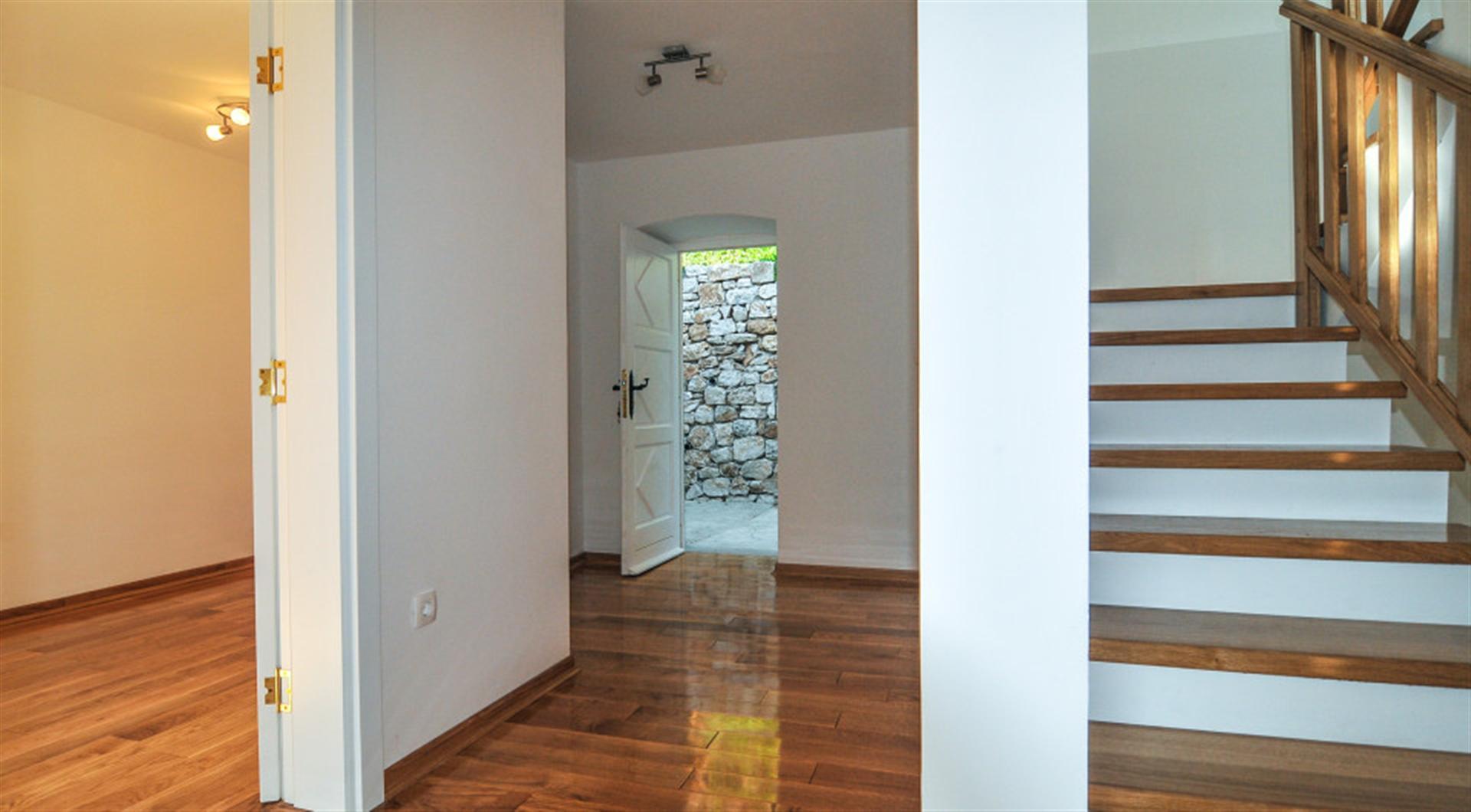 Villa interior in Dražin Vrt, Montenegro: a bright hall with a wooden staircase, parquet flooring, and access to a stone wall.