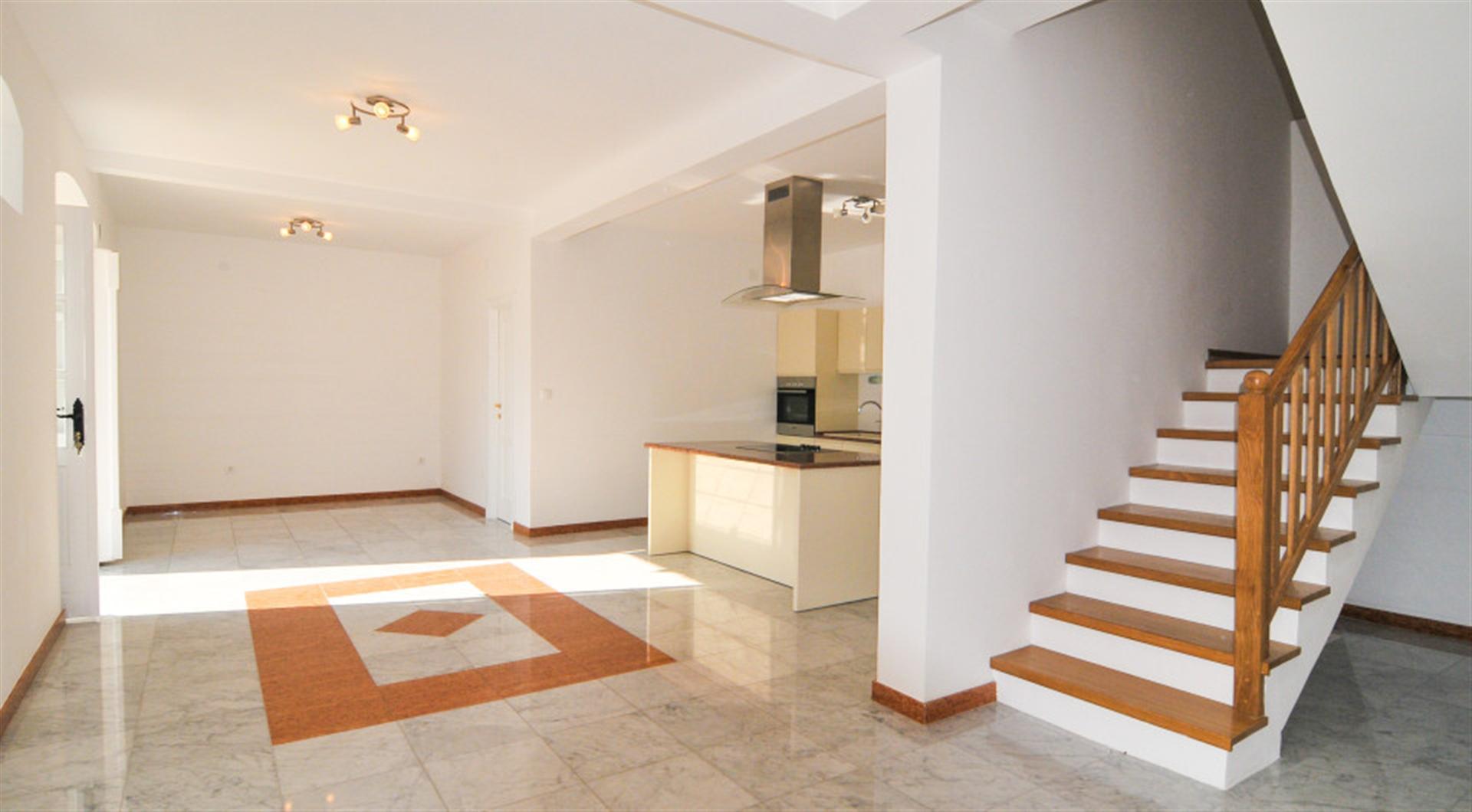 Spacious living room with kitchen and wooden staircase in a villa in Dražin Vrt, Montenegro: bright interior, tiled floor.
