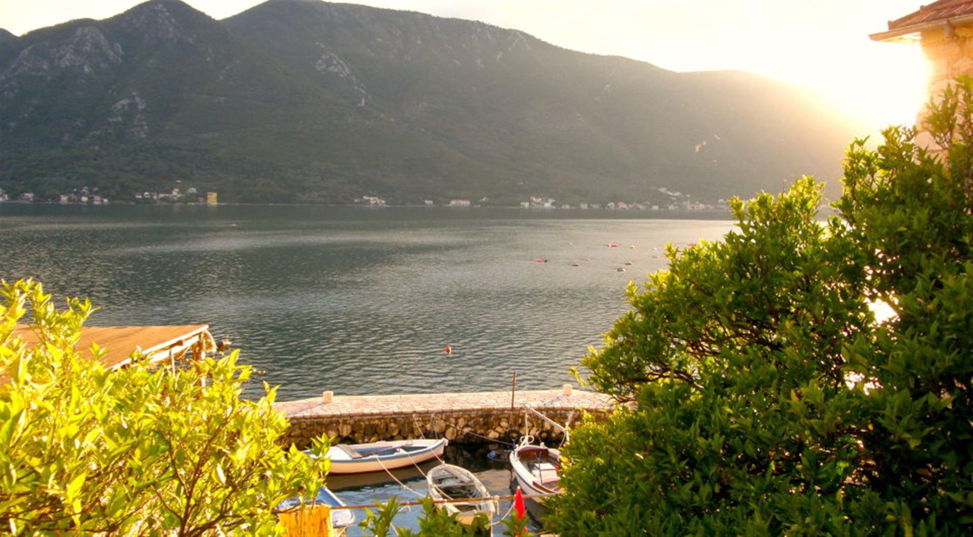 View of the Bay of Kotor and mountains from the villa terrace in Dražin Vrt, Montenegro: a pier with boats and greenery in the foreground.