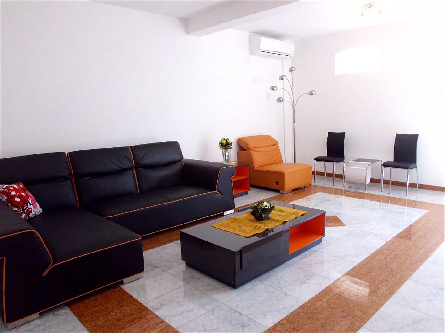 Living room in a villa in Drazin Vrt, Montenegro: black leather sofa, orange armchair, coffee table, and marble floor.