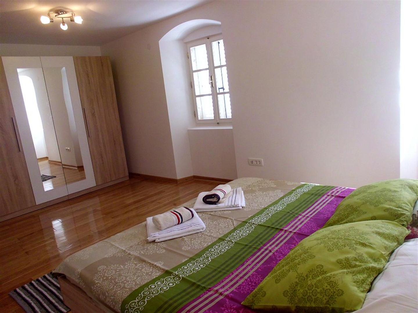 Bedroom with a double bed and wardrobe in a villa in Drazin Vrt, Montenegro: bright interior, parquet flooring, and an arched window.
