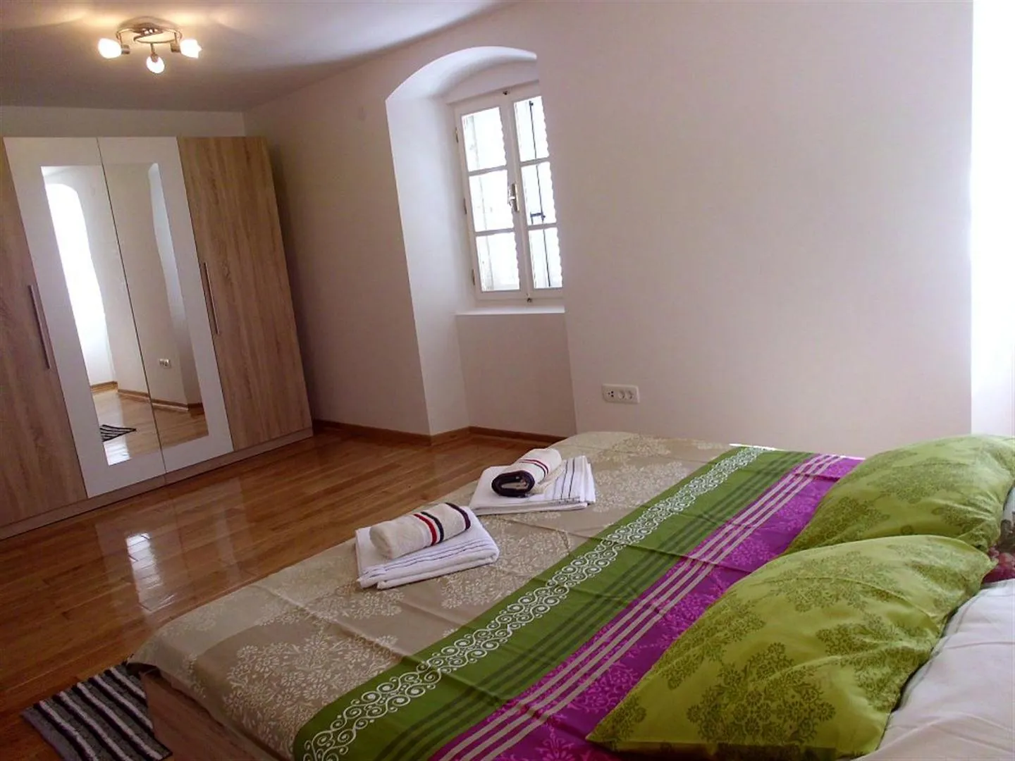 Bedroom with wooden floors, a bed featuring colorful bedding, and a large wardrobe with mirrored sliding doors.
