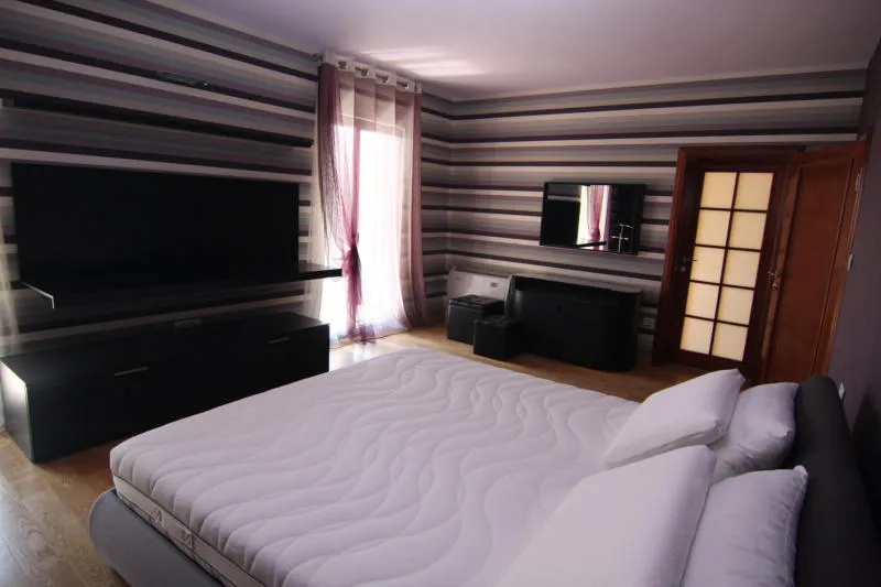 Bedroom featuring a large bed, striped wallpaper, and a wall-mounted TV.
