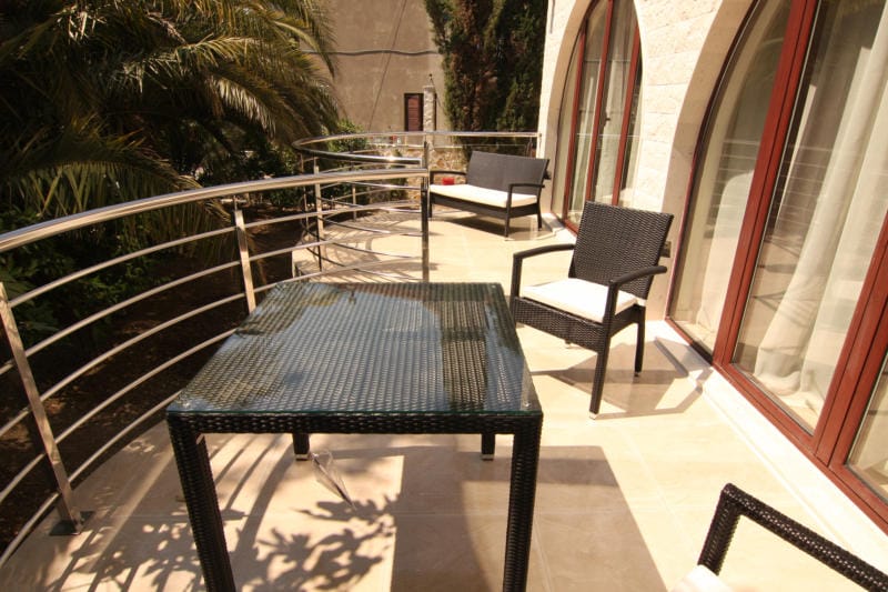 Spacious villa terrace in Lastva, Montenegro: wicker furniture, glass table, and stainless steel railing.