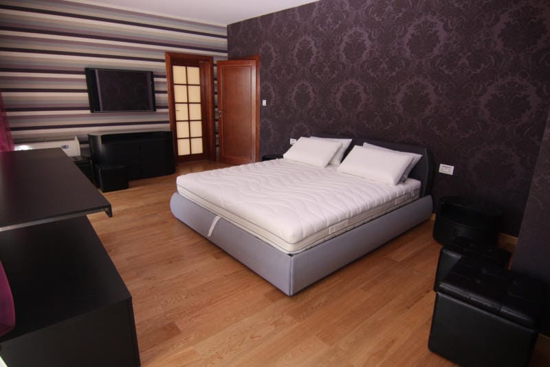 Spacious bedroom with a double bed in a villa, Lastva, Montenegro: dark wallpaper, wooden floor, and modern furniture.