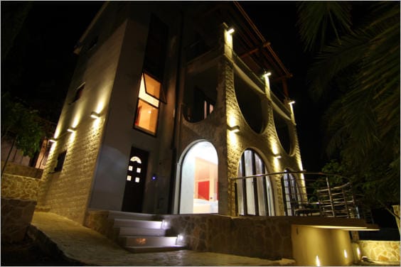 Three-story villa in Lastva Grbaljska, Montenegro: nighttime facade lighting, stone cladding, and arched terraces.