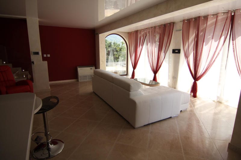 Living room with a white sofa and panoramic windows in a villa in Lastva, Montenegro: modern interior with red walls.