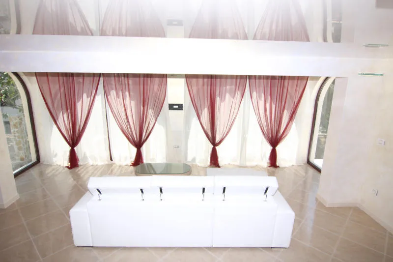 White sofa and red curtains in a spacious room with arched windows and tiled floor.