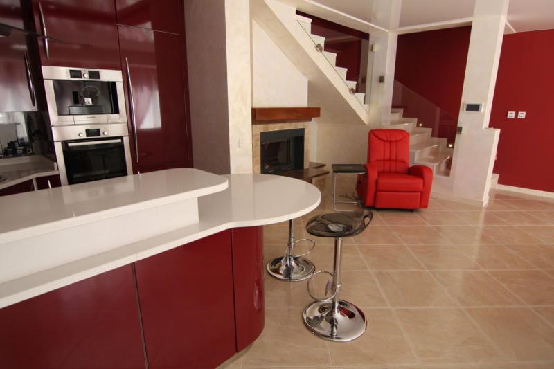 Modern kitchen with a burgundy kitchen set, a bar counter, and a fireplace in a villa in Lastva, Montenegro.