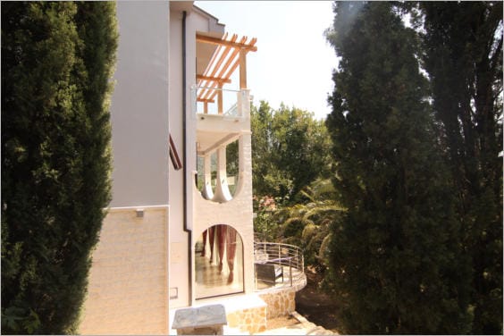 Facade of a modern villa in Lastva Grbaljska, Montenegro: arched terraces, panoramic windows, and a garden with cypress trees.