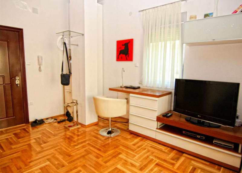 Living room with parquet flooring, TV stand, and desk in an apartment in Bečići, Montenegro. Bright interior with furniture.