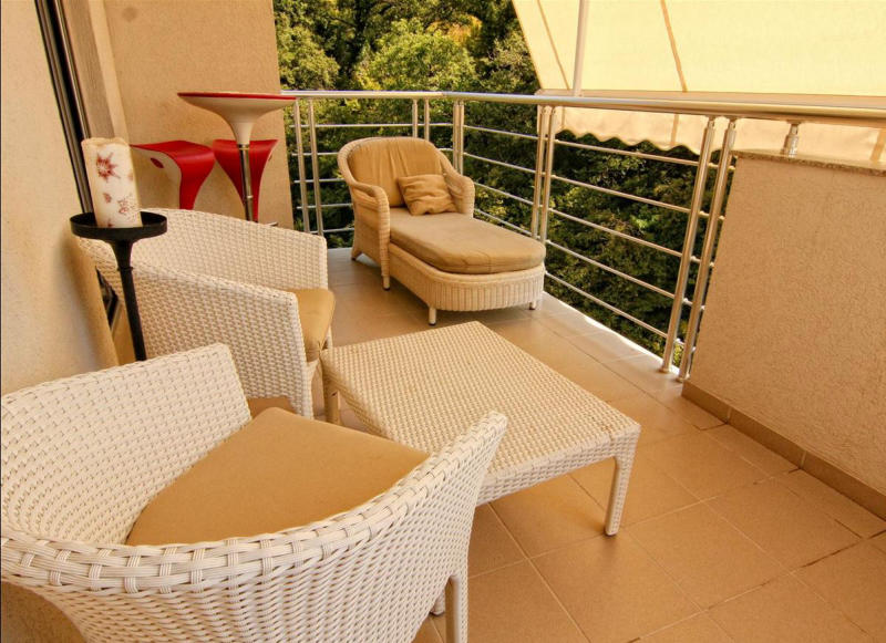 Cozy terrace with wicker furniture and a view of greenery in an apartment in Bečići, Montenegro. Balcony with a sun awning.