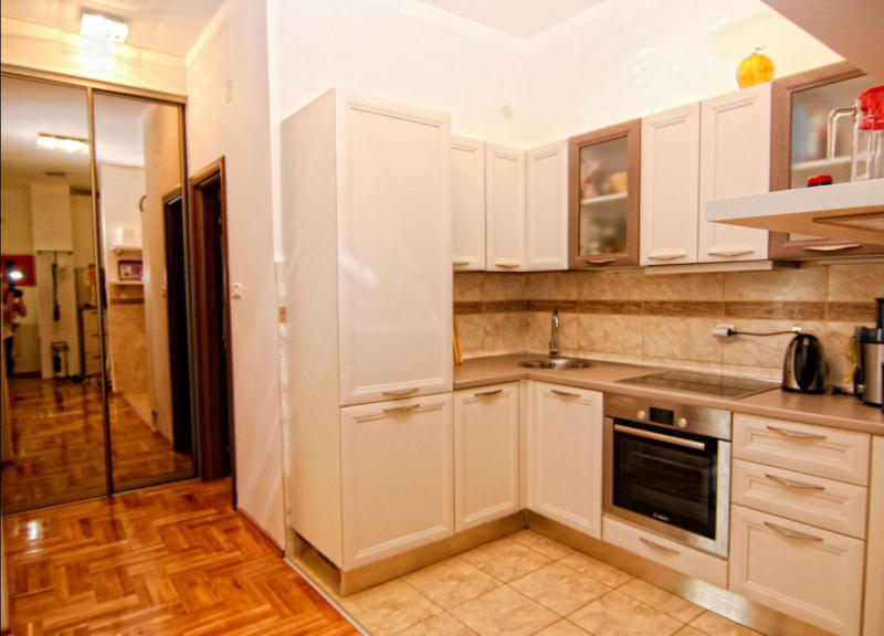 Bright corner kitchen in an apartment in Becici, Montenegro: built-in appliances, white fronts, and a mirrored sliding wardrobe.