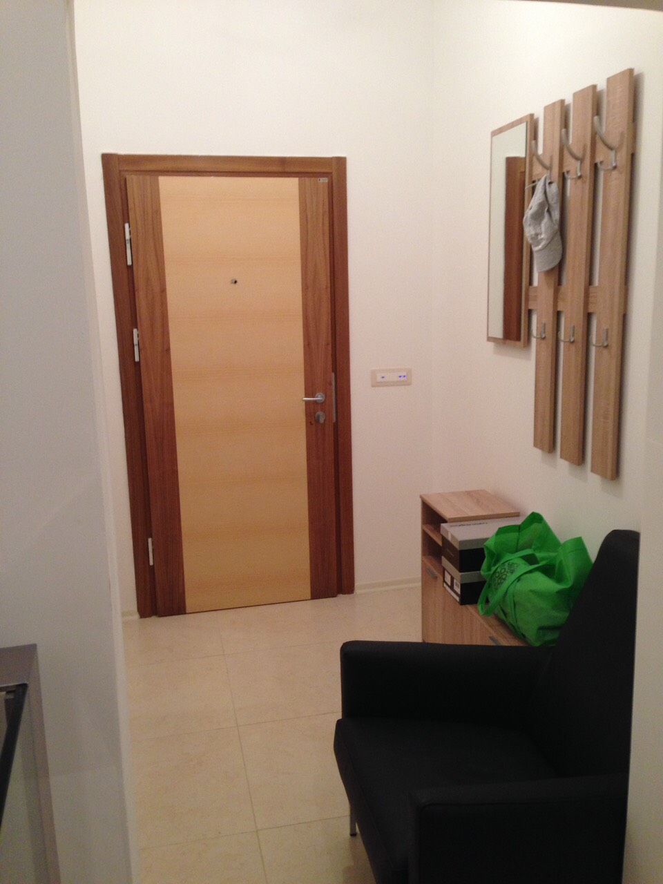 Hallway in an apartment in Bečići, Montenegro: light finishes, wooden front door, coat rack with mirror, and an armchair.