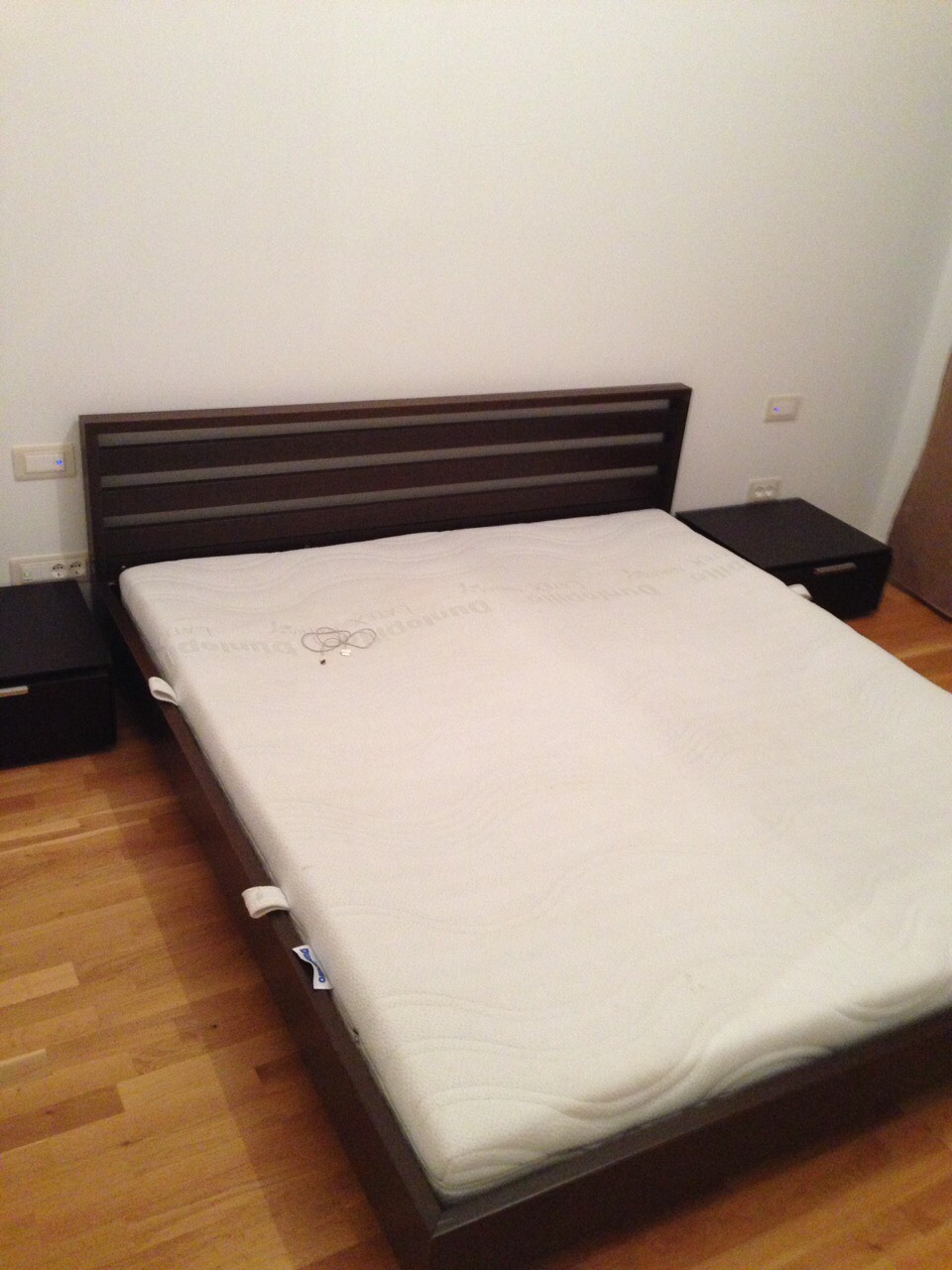 Double bed with a dark headboard and nightstands in the bedroom of an apartment in Becici, Montenegro. Parquet flooring.
