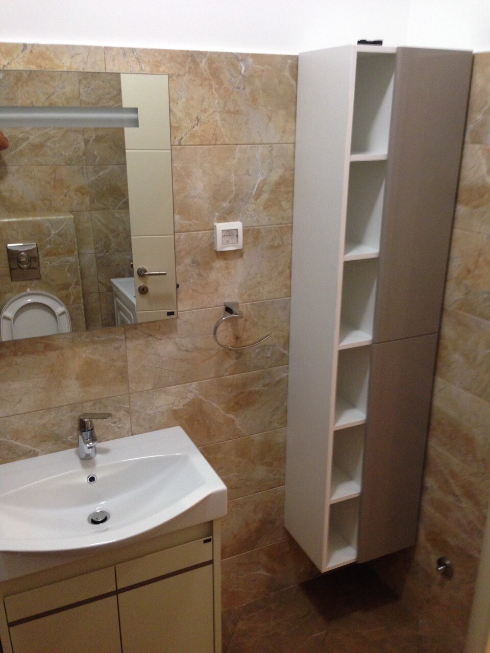 Bathroom in an apartment in Bečići, Montenegro: white sink, wall-mounted cabinet, and beige tiled wall finish.