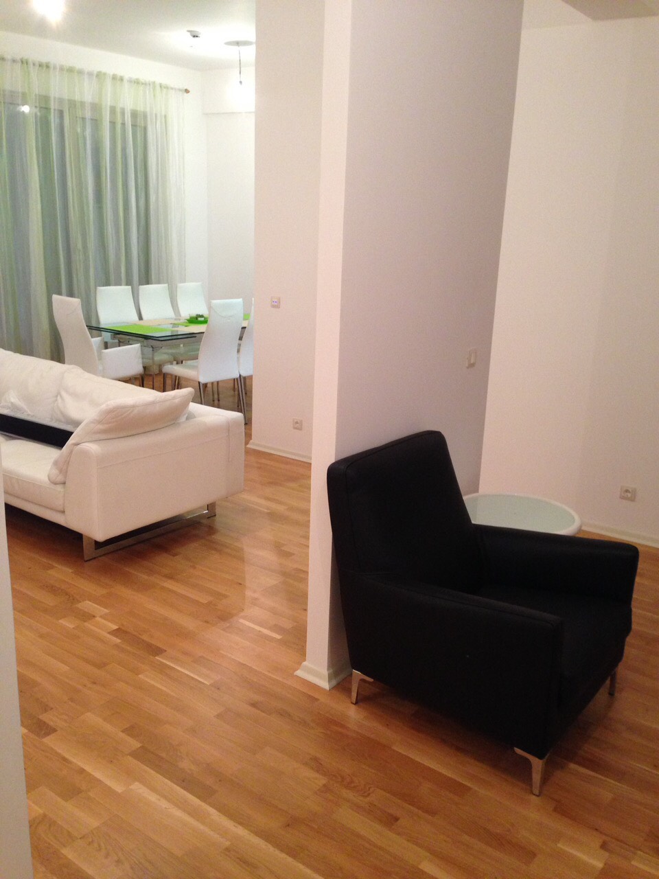 Modern living room with a white sofa and dining area in an apartment in Bečići, Montenegro, parquet flooring and a bright interior