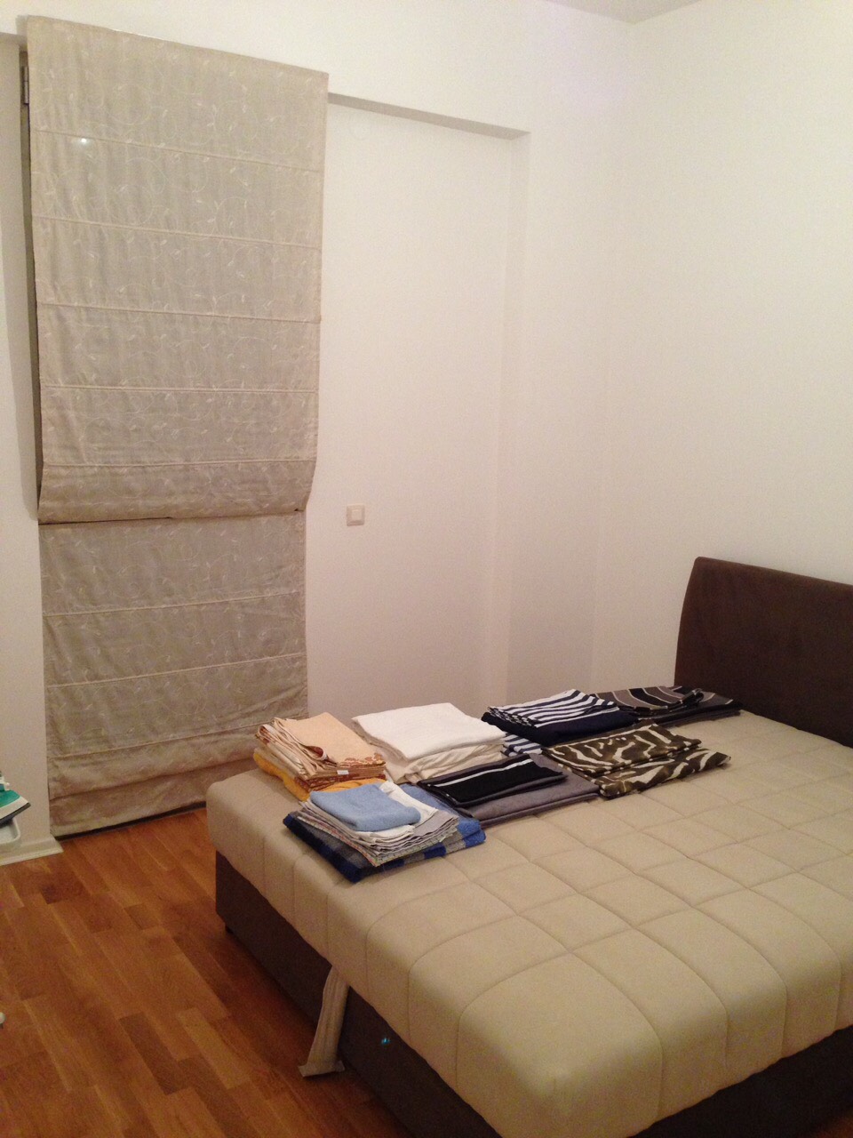Bedroom in an apartment in Bečići, Montenegro: a double bed with a soft headboard, light Roman shades, and parquet flooring.