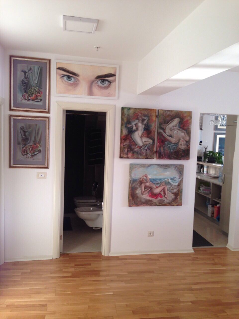 Living room interior with paintings and entrance to the bathroom in an apartment in Bečići, Montenegro: light walls, parquet floor.