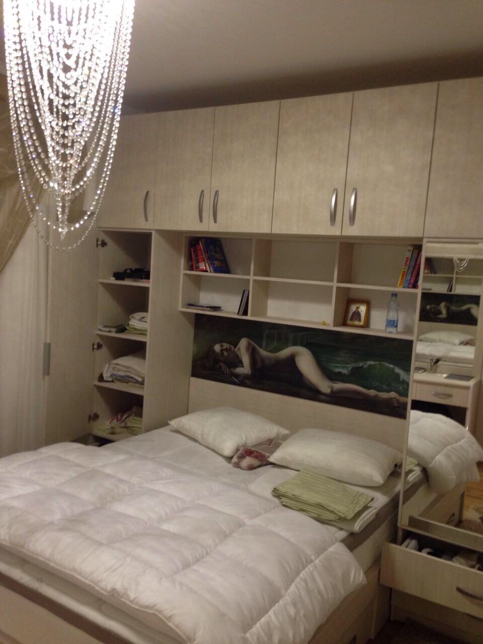 Bedroom in an apartment in Bečići, Montenegro: double bed, built-in wardrobe with shelves, and a crystal chandelier.