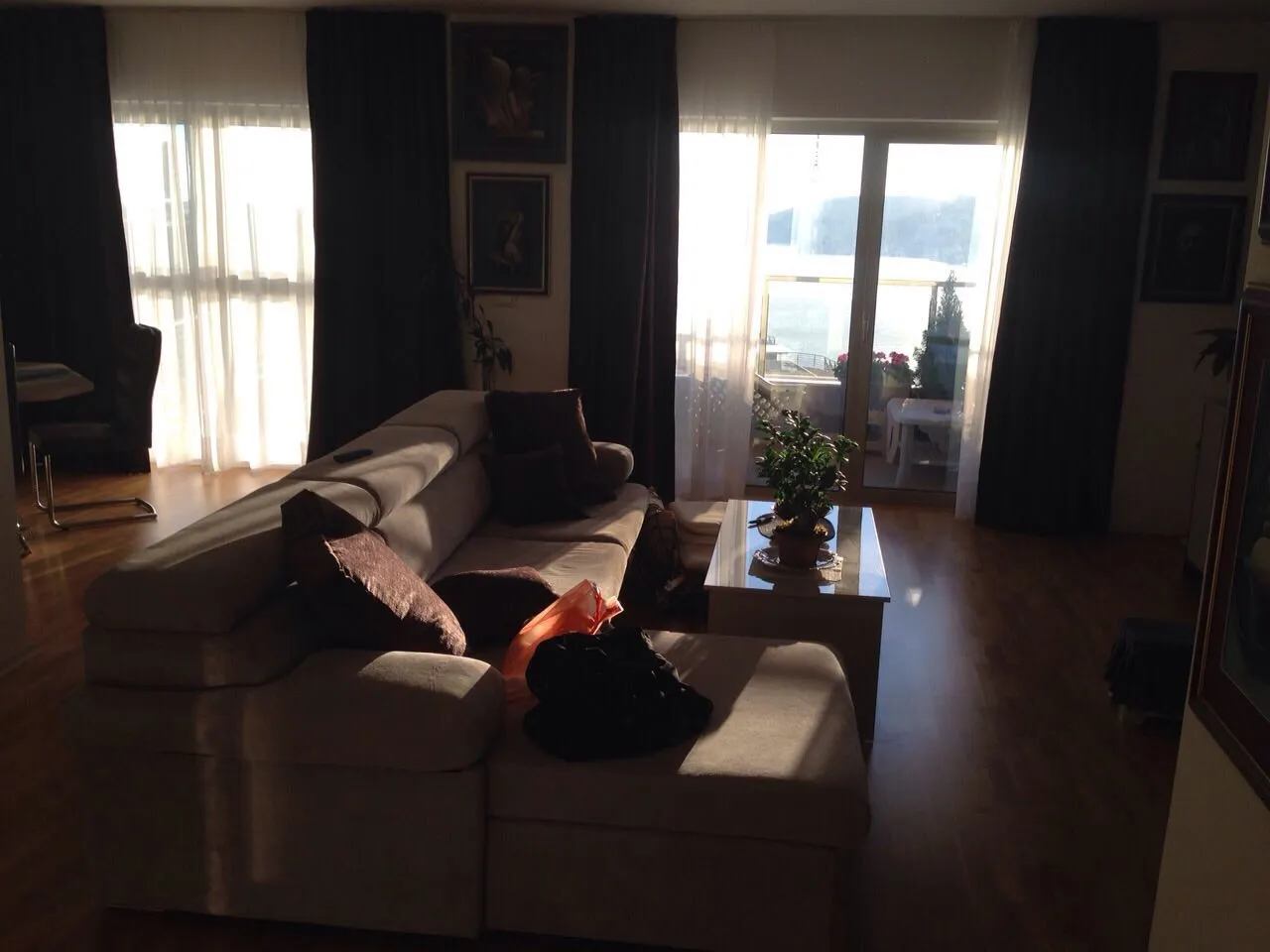 Living room featuring a large beige sofa, coffee table with a plant, and balcony doors with dark curtains.