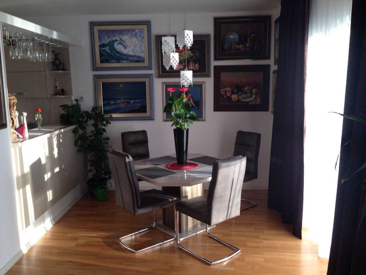 Dining area in the apartment living room in Bečići, Montenegro: table, leather chairs, wall art, and a bar counter.
