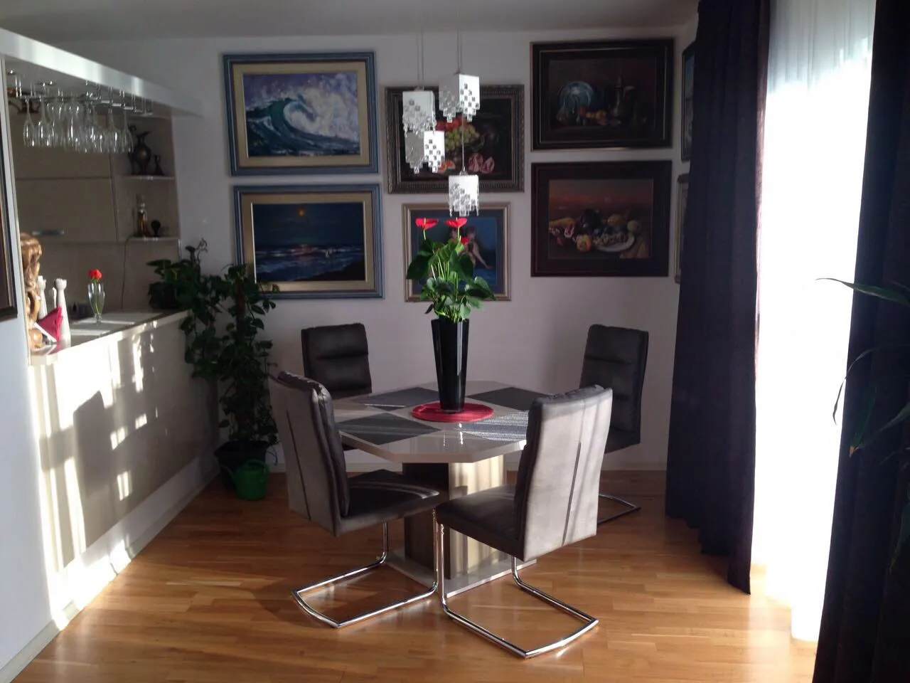 Dining area with a table, four chairs, framed art on the wall, and a bar counter visible on the left.