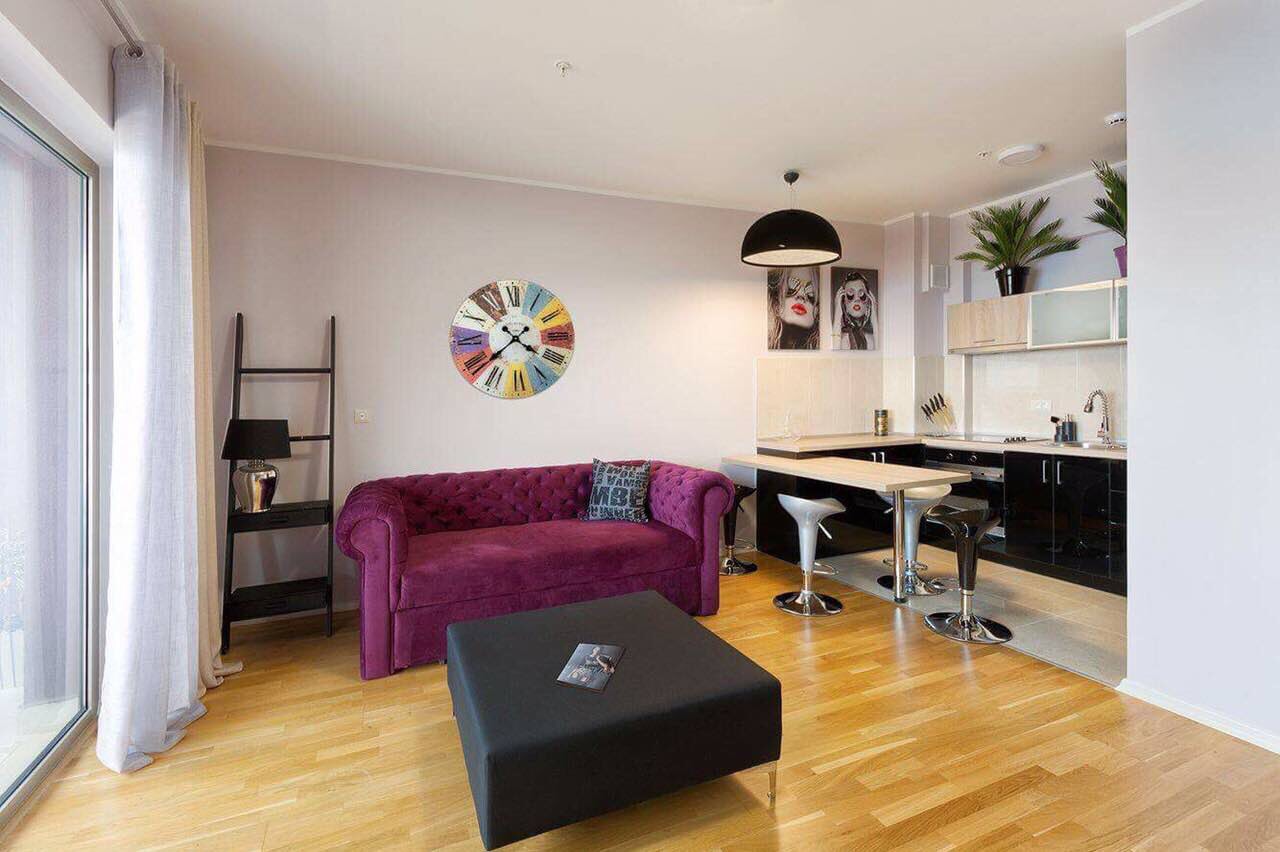 Modern living room with a purple sofa and kitchen in an apartment in Bečići, Montenegro: stylish interior with parquet flooring.