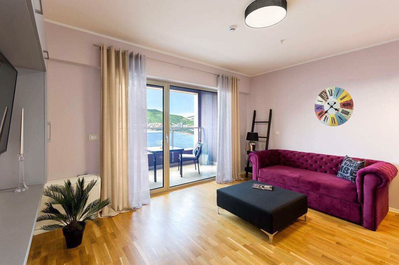 Living room in an apartment in Bečići, Montenegro: purple sofa, panoramic sea view, and access to the terrace.
