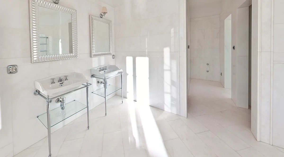 Two white pedestal sinks with chrome stands and framed mirrors on white marble tiled walls.