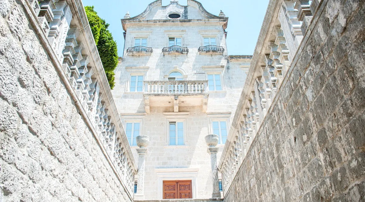 Low angle view of a historic stone building facade featuring balconies and a grand staircase.