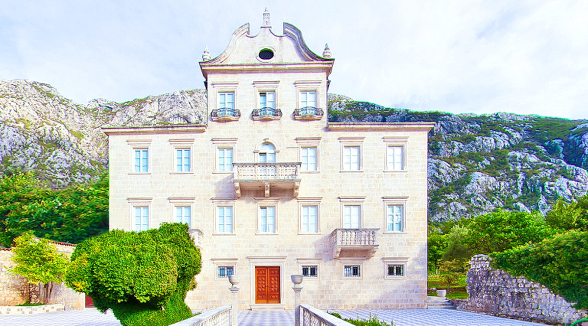 Historic stone villa in Dobrota, Montenegro: building facade with balconies against a mountain backdrop.